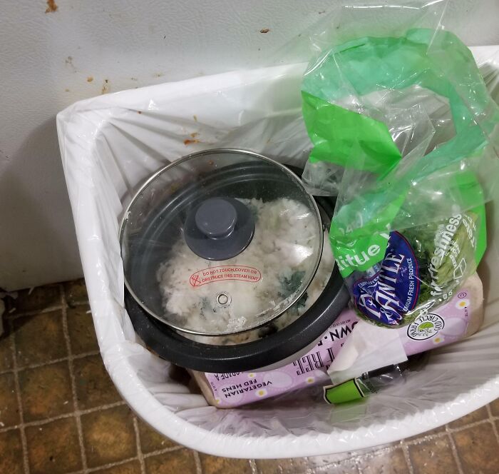 Rice cooker with leftover food discarded in a trash bin shows awful roommates neglect and mess in shared living space.