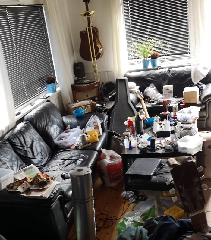Cluttered living room with messy couches, musical instruments, scattered items, and various household clutter left by awful roommates.