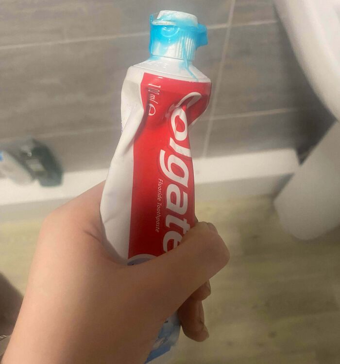 Hand holding a flattened Colgate toothpaste tube, showing one of the awful roommate habits in shared bathroom spaces.
