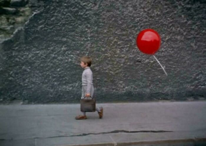 Young boy walking with a briefcase and a red balloon floating behind him, evoking nostalgia and feeling old as heck.