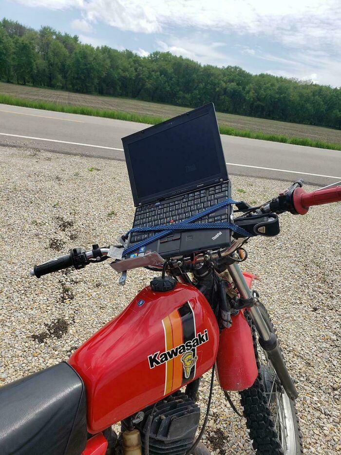 Laptop secured to the handlebars of a Kawasaki dirt bike showcasing ingenious redneck engineer creativity outdoors.