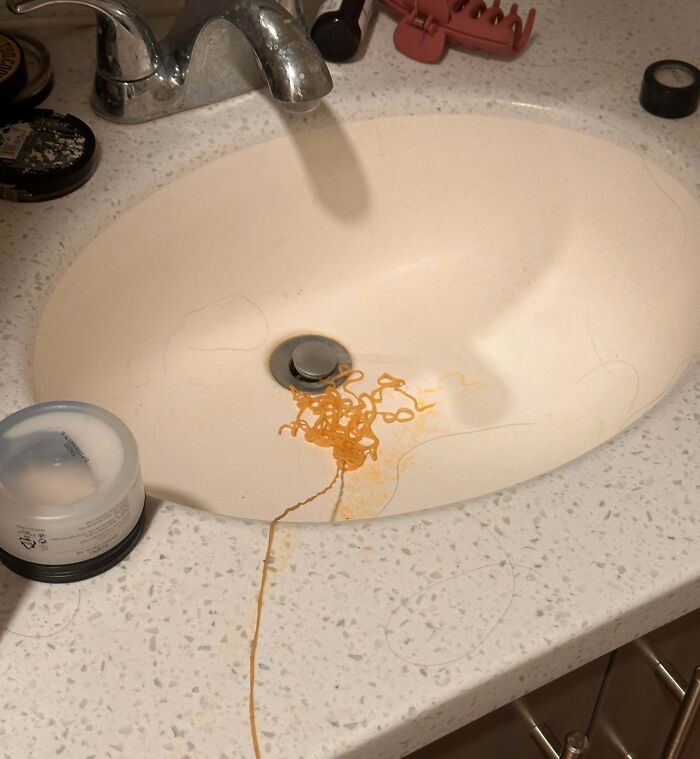 Bathroom sink with uncooked noodles and hair tangled around the drain, showing awful roommate messes.