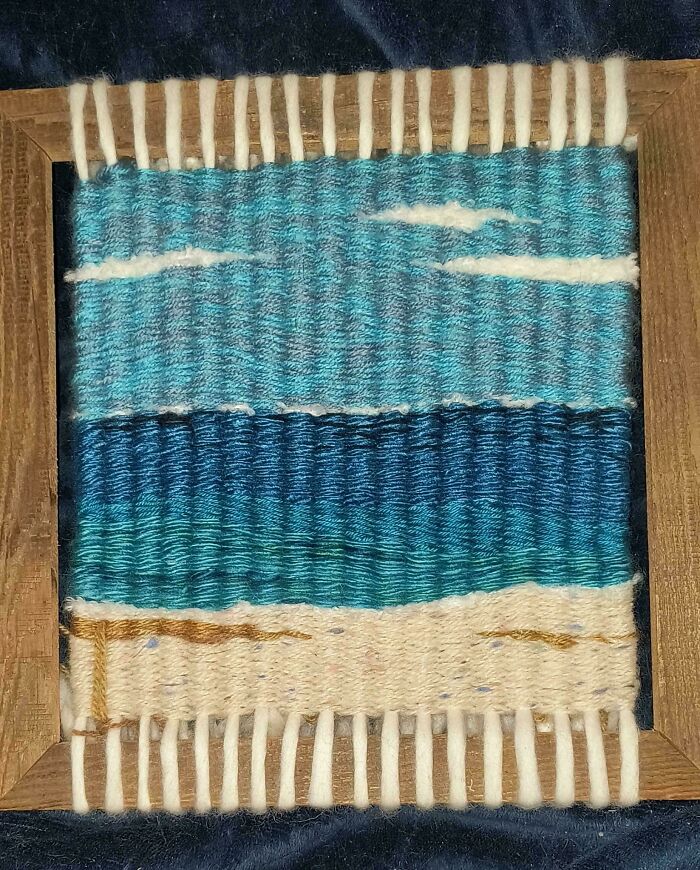 Woven wall art with blue and white yarn depicting a calm ocean scene, showcasing the wholesome creativity of moms.