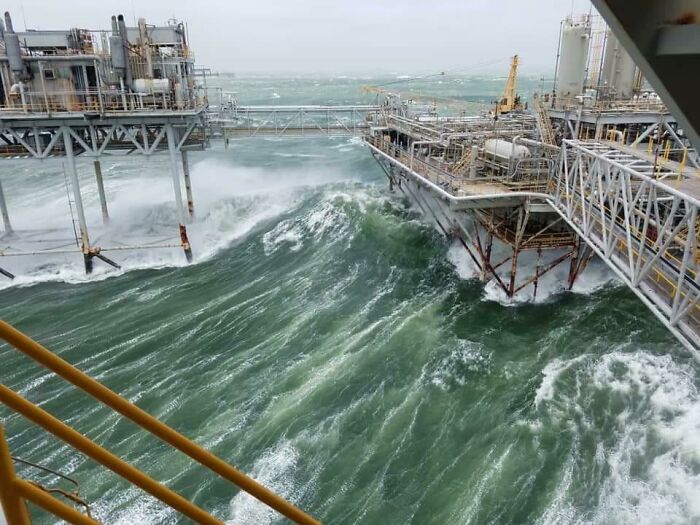 Rough ocean waves crashing against an offshore oil rig, showcasing one of the jobs that should pay more.