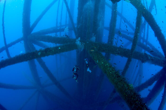 Underwater divers inspecting large metal structure, illustrating jobs that should pay more based on unsettling worker photos.