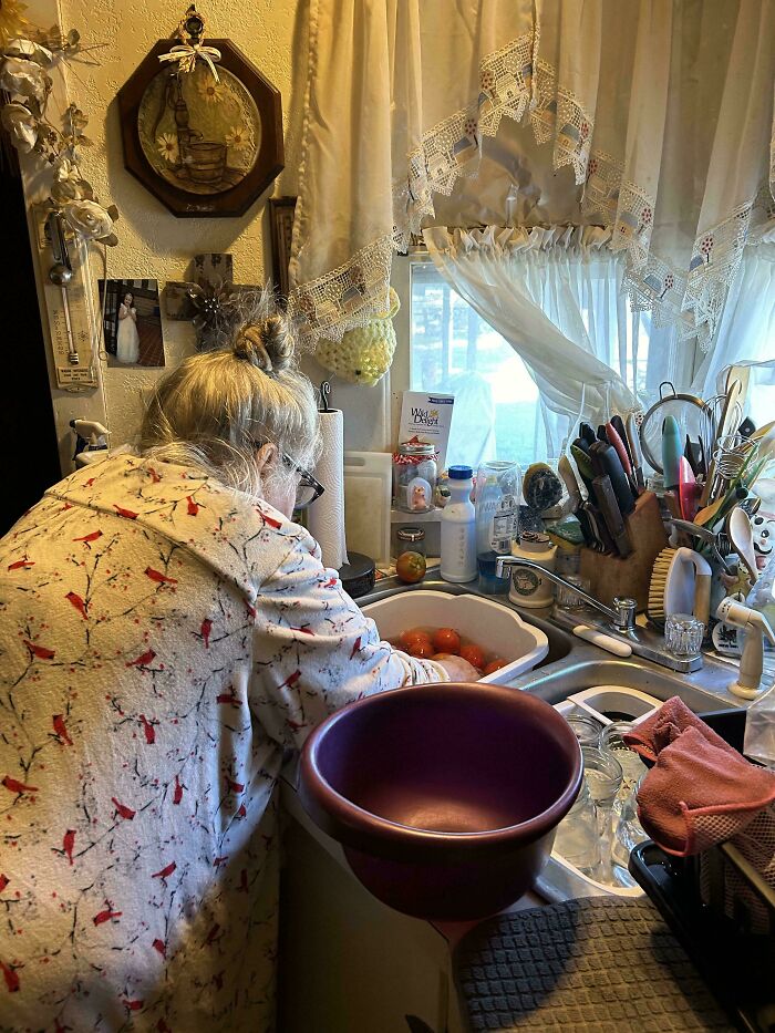 Elderly mom washing tomatoes at the kitchen sink, showcasing wholesome moments of moms being their amazing selves.