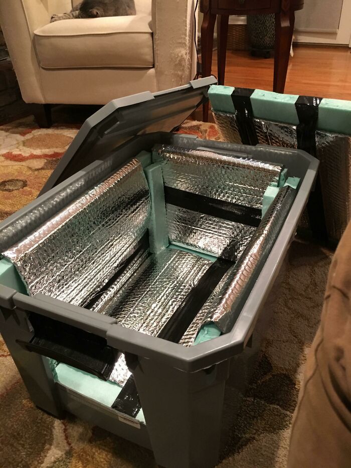 Plastic cooler box lined with reflective insulation foil and foam for temperature control indoors on a carpet.