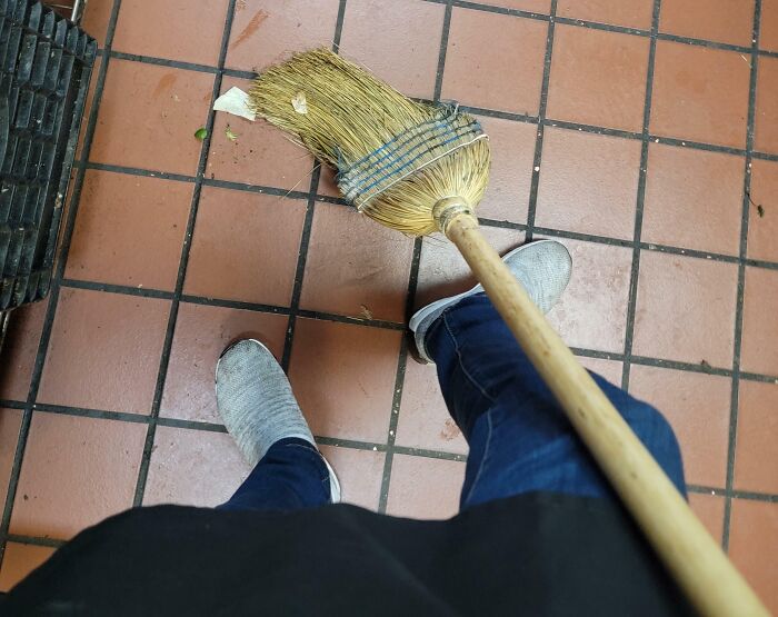 Person sweeping a tiled floor wearing casual shoes, illustrating reasons people hate their boss with cleaning tasks.