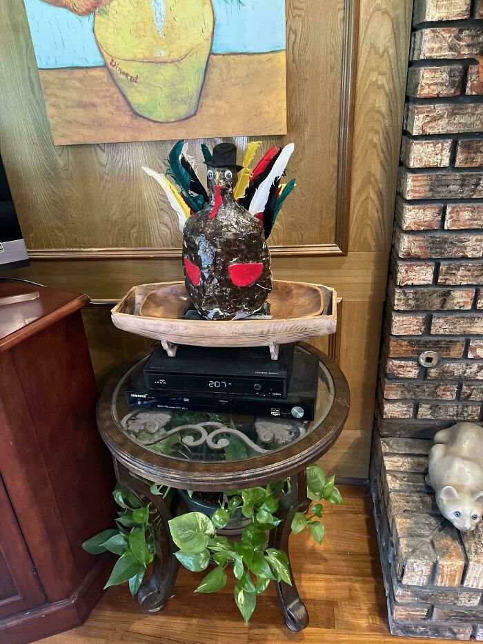 Handcrafted decorative turkey with colorful feathers on a wooden tray atop a round glass table with green plants nearby.
