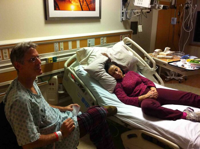 Mom resting in hospital bed with a man sitting beside her, capturing a wholesome moment of moms being their amazing selves.