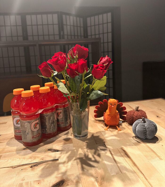 Vase of red roses, orange Gatorade bottles, and autumn-themed decorations on a wooden table, evoking wholesome moms vibes.