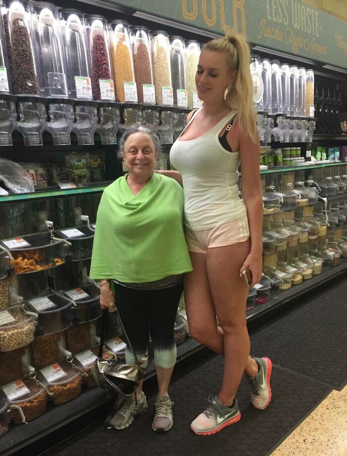 Two women in casual clothes at a store aisle filled with bulk dry goods, showcasing funny parents in a lighthearted moment.