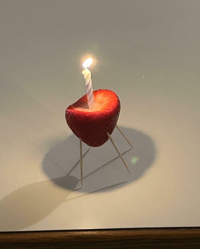 Strawberry with a lit birthday candle supported by toothpicks, showcasing one of the funniest parents ever creative ideas.