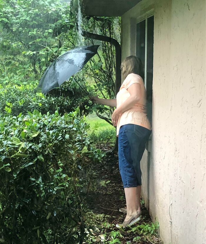 Woman holding an umbrella to catch rainwater, showcasing a wholesome moment of moms being their amazing selves outdoors.