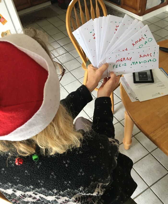 Mom wearing a Santa hat holding Christmas cards at a kitchen table, showcasing wholesome moments of moms being amazing.