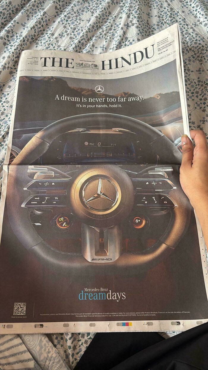 Hand holding a newspaper with a smart Mercedes-Benz steering wheel design shown in an innovative car ad.