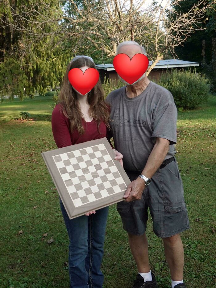 Two people outdoors proudly holding a handcrafted wooden chessboard showcasing woodworking skills and craftsmanship.