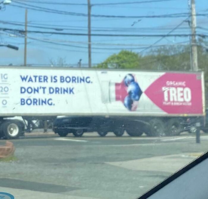 A semi-truck with an ad reading water is boring don't drink boring in a US street scene dystopian setting.