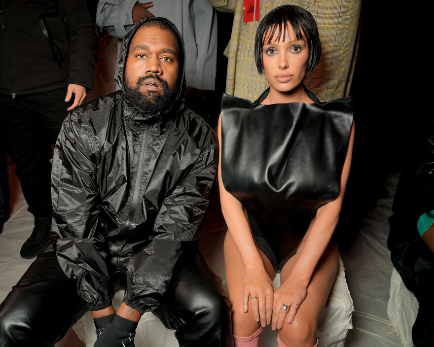 Kanye West and Bianca Censori sitting together at an event, showcasing fashion linked to West’s growing empire. Kanye West and Bianca Censori sitting together at an event, showcasing fashion linked to West’s growing empire.