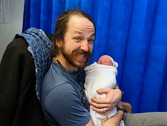 Smiling father holding newborn baby wrapped in blanket, capturing a funny and wholesome parenting moment.