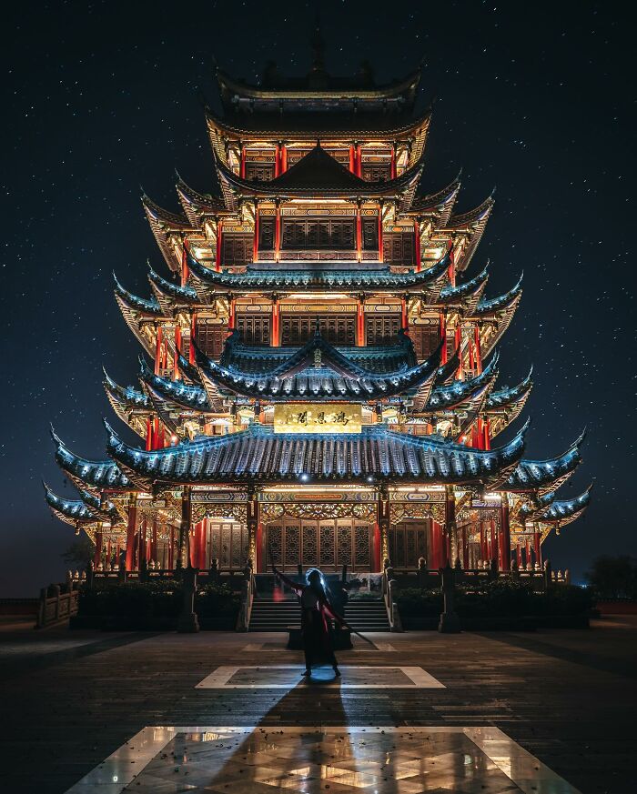 Traditional Asian pagoda illuminated at night with a person standing in front, showcasing glimpses of everyday life in Asia.