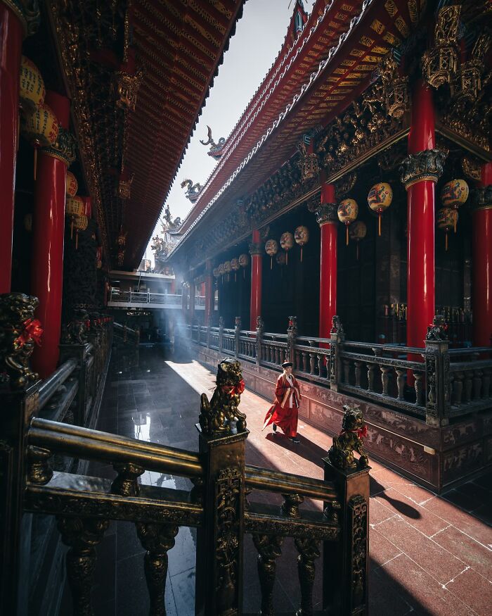 Traditional Asian temple courtyard with red pillars and a person walking, showcasing glimpses of everyday life in Asia.