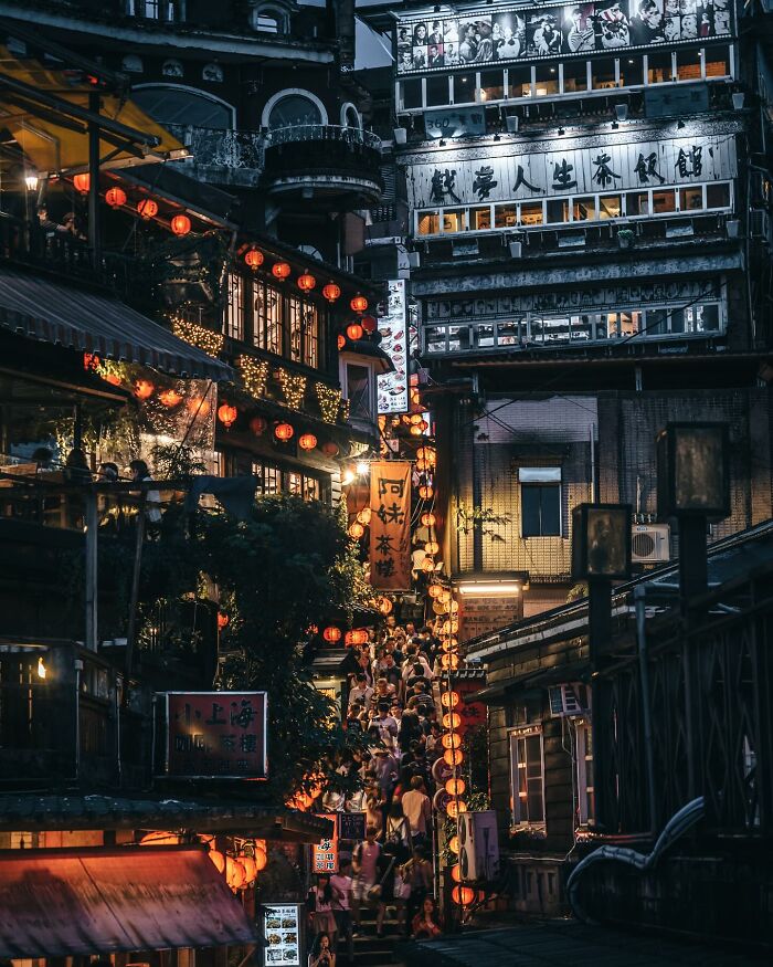 Crowded narrow street in Asia illuminated by warm lanterns and bustling with people capturing everyday life scenes.