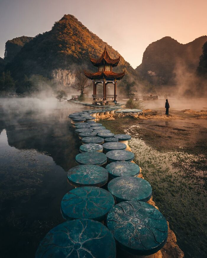Scenic glimpse of everyday life in Asia with traditional pavilion, stone path, and misty mountains at sunrise.