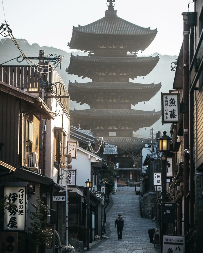 Traditional pagoda and narrow street scene showcasing everyday life in Asia with people walking on a quiet path.