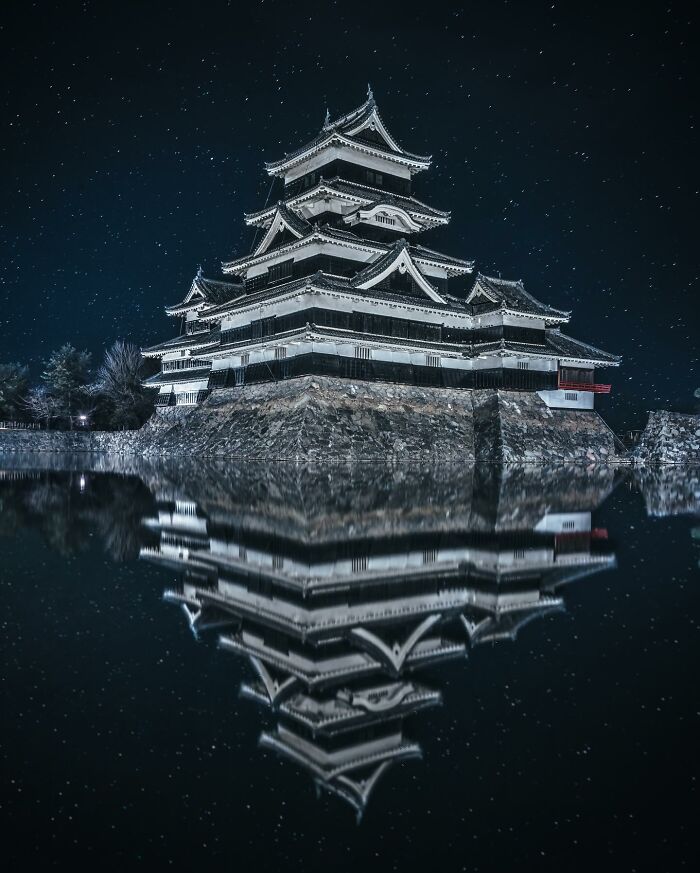 Traditional Japanese castle at night reflected in water, showcasing glimpses of everyday life in Asia photography.