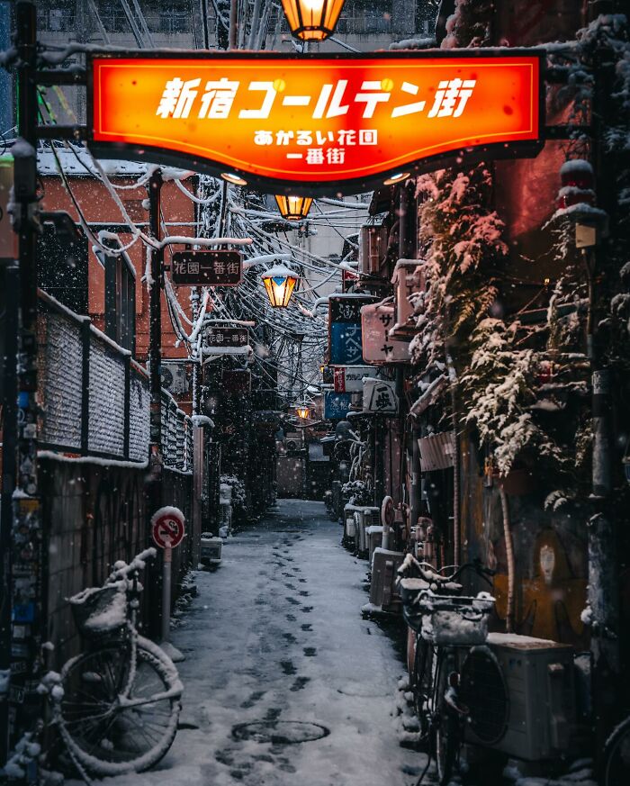 Snow-covered narrow street in Asia with bicycles and glowing lanterns, capturing everyday life in a quiet moment.