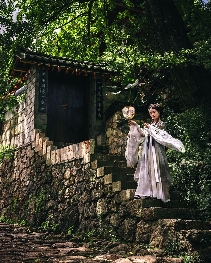Woman in traditional clothing holding a fan on stone steps, showcasing glimpses of everyday life in Asia photography.