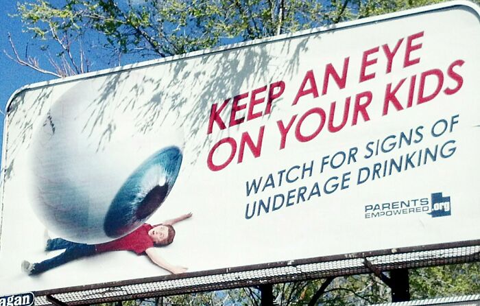 Billboard showing a giant eyeball rolling over a child with a warning about underage drinking.