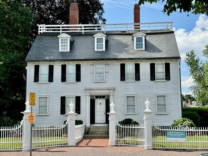 Historic white colonial house with black shutters and fenced yard, one of the iconic TV houses real in life.