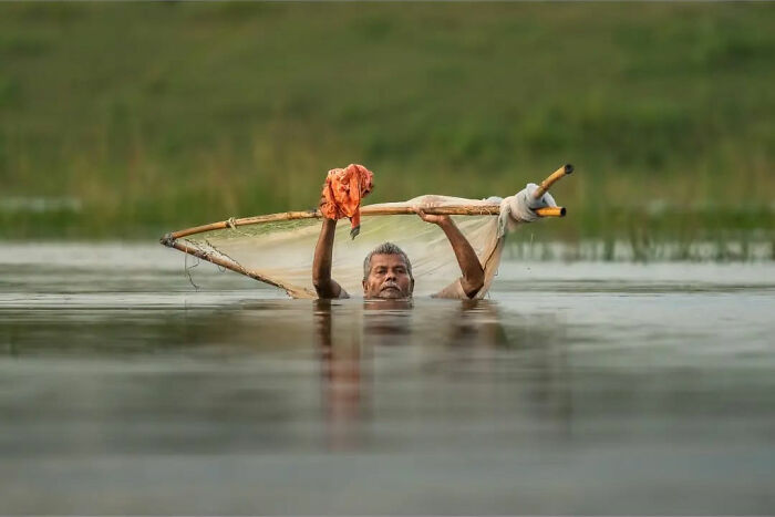 Man in water holding fishing net, capturing everyday life in India with traditional fishing methods.