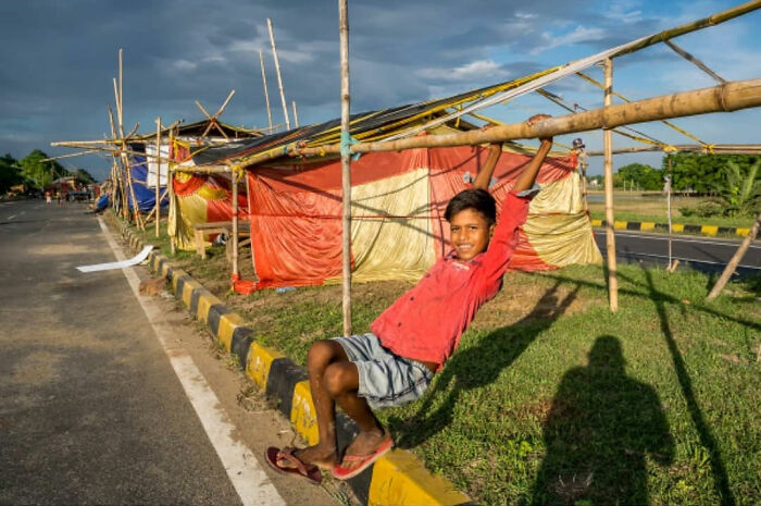 Boy in a red shirt playing on bamboo structure beside road, capturing everyday life in India with vibrant street scenes.