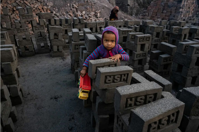 Young child playing with a toy truck among concrete bricks, capturing everyday life in India through photography.