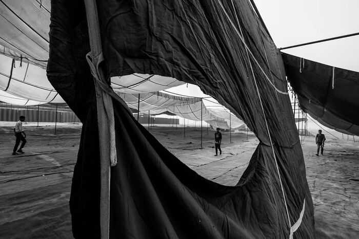 Black and white image showing people walking under large tents, capturing everyday life in India through photography.