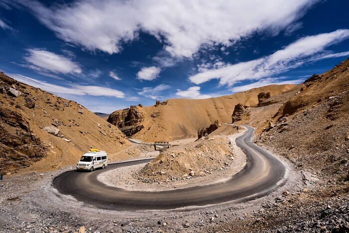 White van driving on a winding mountain road under a vibrant sky, capturing everyday life in India.