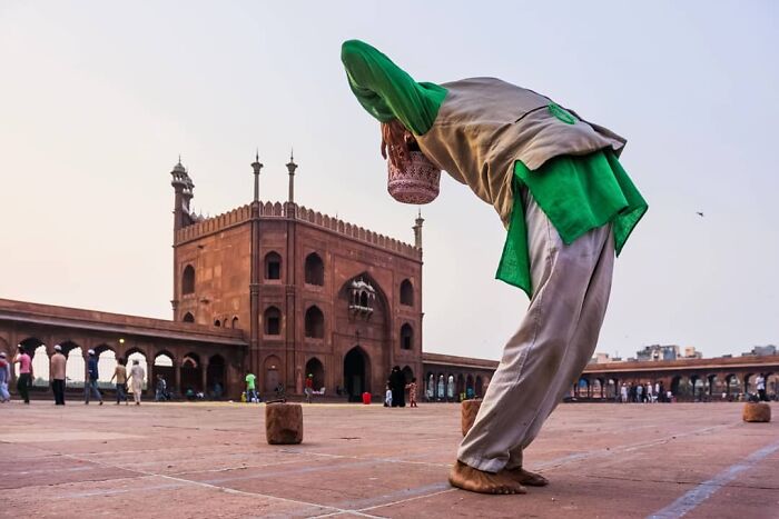 Man performing prayer in traditional clothing at a historic site, showcasing everyday life in India captured by photographer.