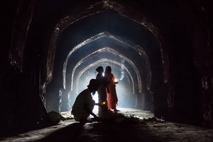 Silhouettes of people lighting candles inside an ancient archway depicting everyday life in India.
