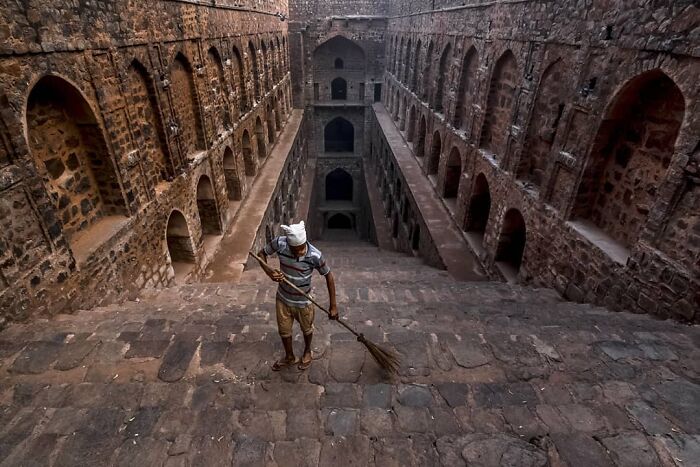 Man sweeping stone steps at historic stepwell, capturing everyday life in India with ancient architecture surrounding him.