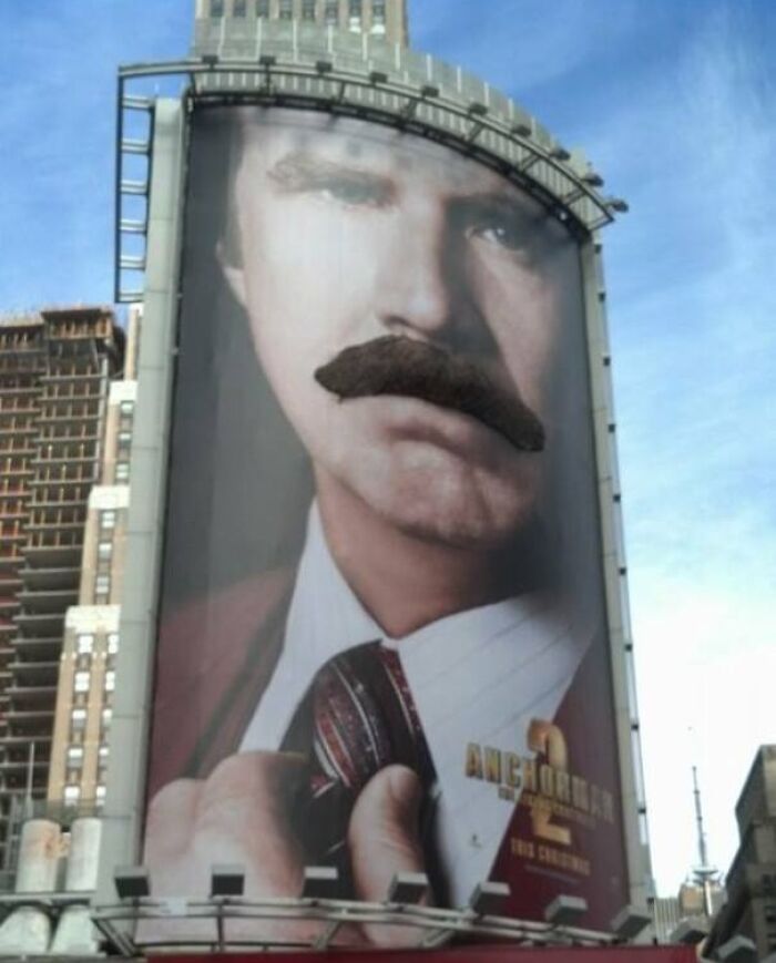 Gigantic funny billboard featuring a man with an oversized fake mustache in an urban cityscape.