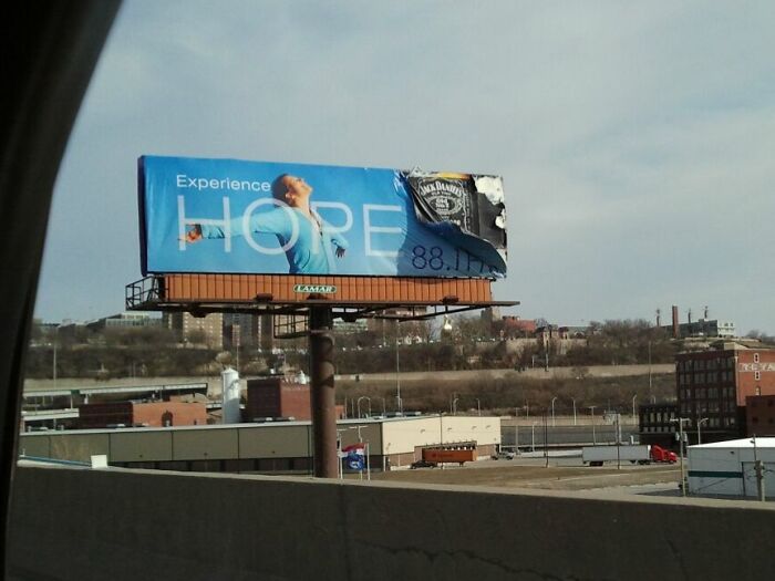 Partly torn billboard showing a hopeful message and a whiskey ad, illustrating funny and weird billboards someone paid for.