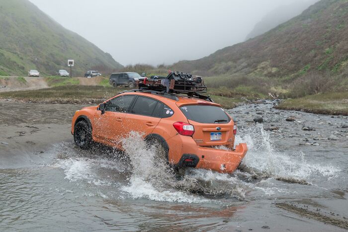 Orange SUV driving through water with splash in misty mountainous terrain, capturing the moment before disaster struck rope broke.