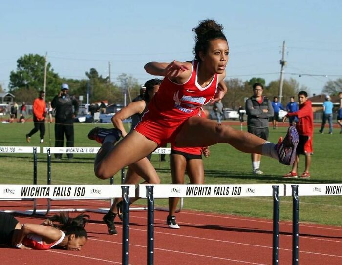 Track athlete clearing a hurdle while another just moments before falling, capturing the moment before disaster struck.