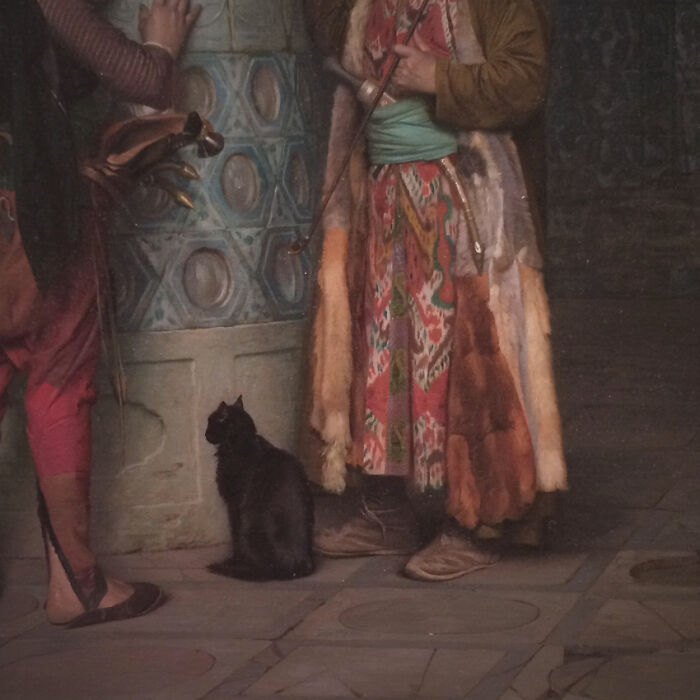 Medieval cats sitting near people dressed in period clothing inside a historic building, showcasing ancient human-cat bond.