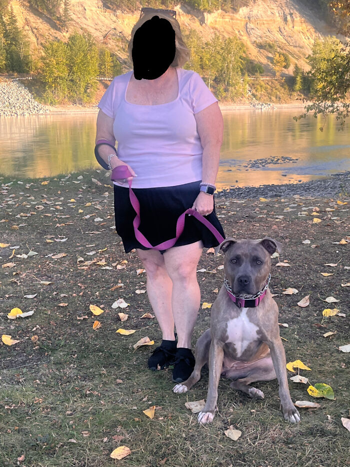Woman standing by a river with her adopted dog on a pink leash, showcasing adorable adopted animals in natural surroundings.