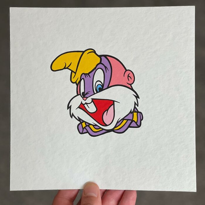 Hand holding a pop mash artwork showing a colorful cartoon character mash-up with vibrant yellow, pink, and purple colors.