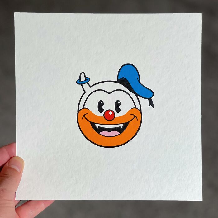 Hand holding artwork of a pop culture and cartoon character mash-up featuring a smiling face with a blue hat and red nose.